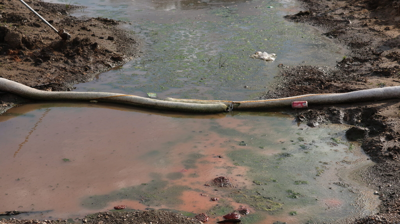 Red, green and black water in the Highway 51 ditch at Smitty's Supply with containment boom separating the black water