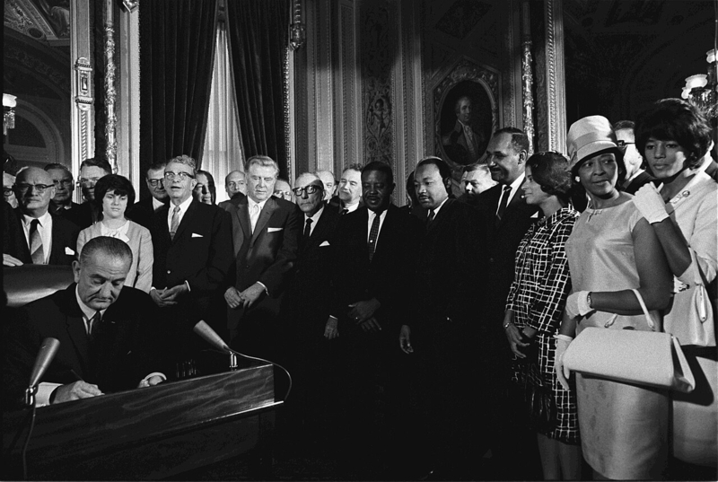 President Lyndon B. Johnson signs the Voting Rights Act of 1965 while Martin Luther King and others look on