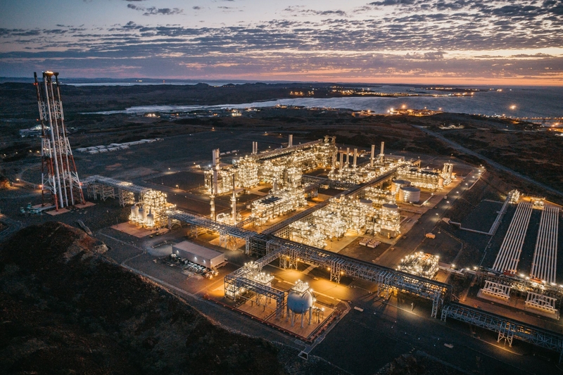 A photo of Woodside Energy’s Pluto liquefied natural gas facility glowing from its lighting at night in Western Australia.