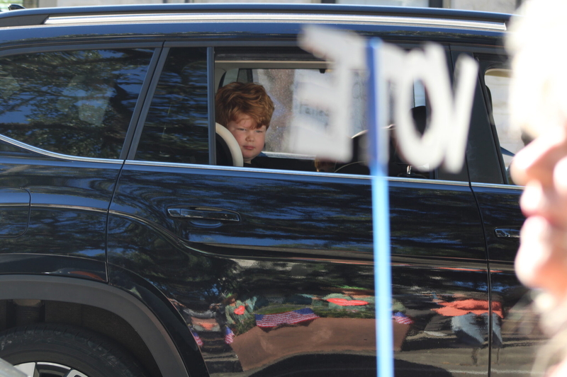 A young boy looks out from the backseat of a vehicle at people taking part in a No Kings rally