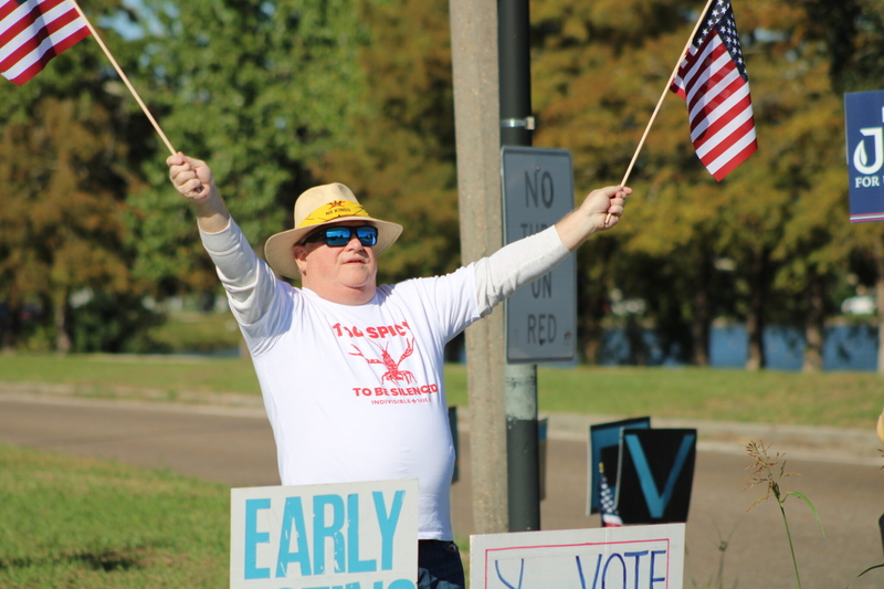 Michael Wolfe spreads his arms to wave American flags. He's wearing a shirt with an image of a crawfish spreading his claws in a similar motion.