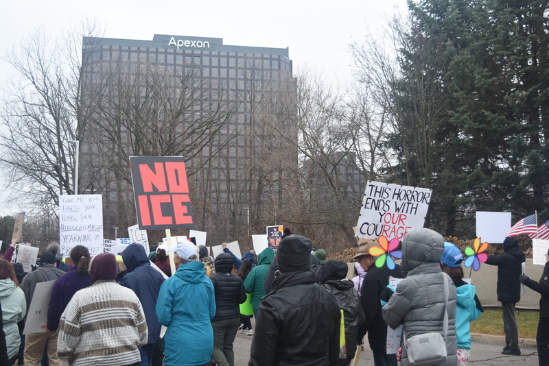 People march towards a tall office building holding anti-ICE signs