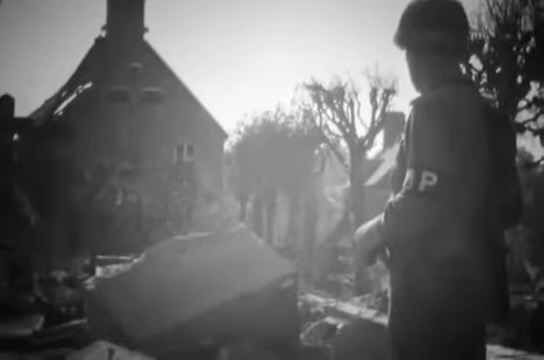 A soldier with the 28th Division stands amid the ruins of Gathemo, France, in August 1944. (Screenshot from National Archives film)