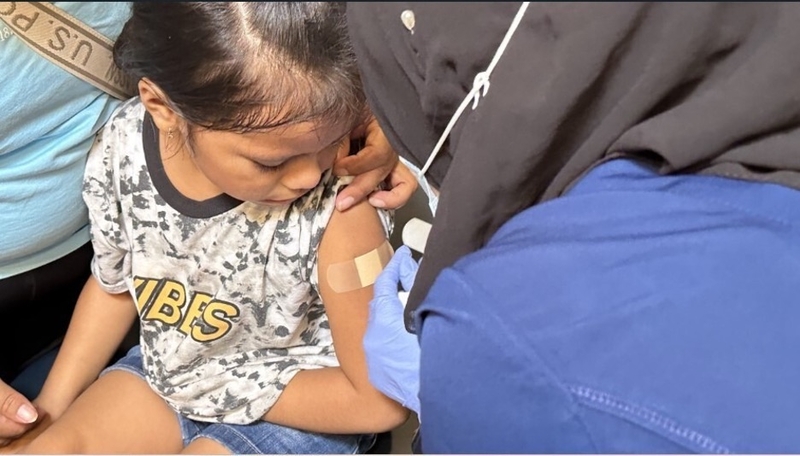 A worker applies an adhesive bandage to a child at a vaccination clinic in Minneapolis’ Corcoran Park in August 2023. Minnesota and other Democratic-led states have sued the federal government over relaxed childhood vaccination standards, and New York has declared a state of emergency as measles cases surge in neighboring Pennsylvania. (Photo courtesy of the City of Minneapolis)