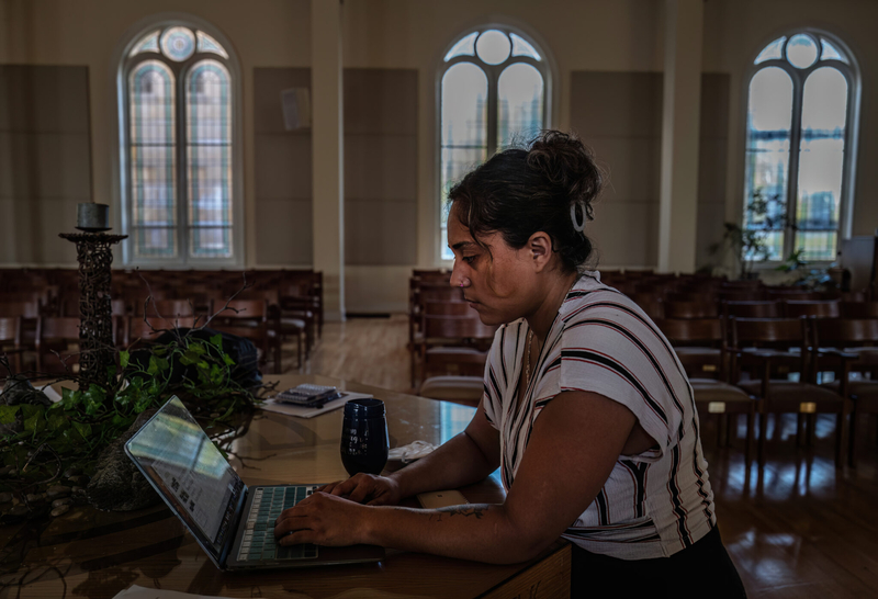 A woman in a short-sleeved blouse types into a computer.