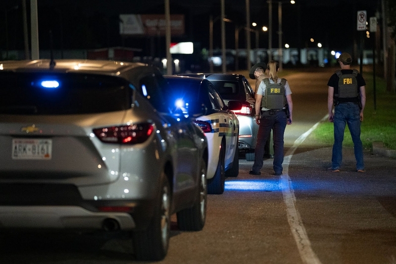 Law enforcement officers stand beside a line of police vehicles.