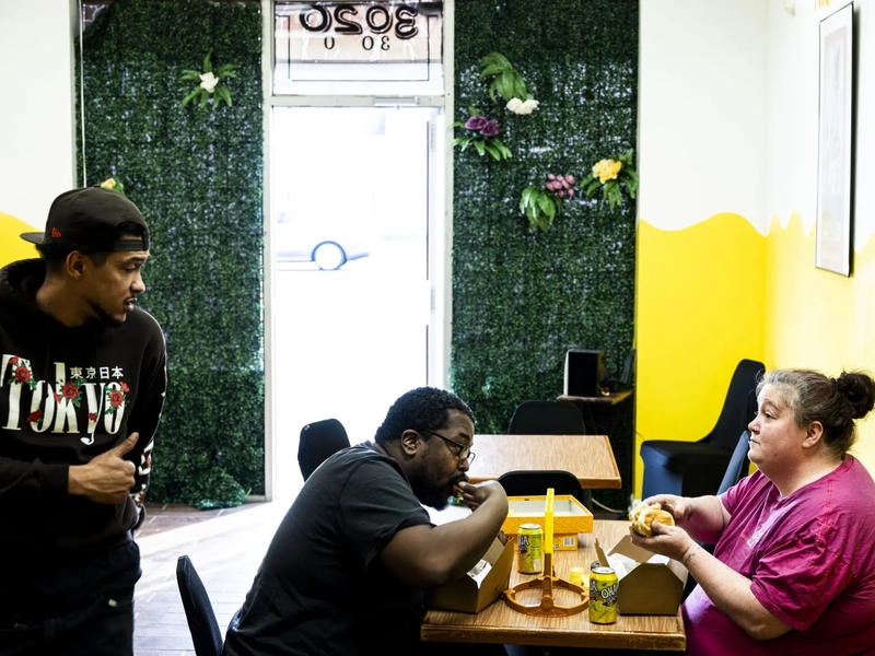 Three people sit at a table and eat sandwiches.
